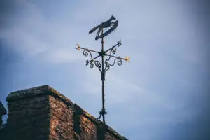 Decorative metal weather vane with directional markers mounted on top of a brick tower at Rowton Castle, set against a soft blue sky, highlighting the historic character of the wedding venue.