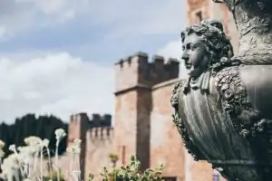 Ornate stone statue in the gardens of Rowton Castle with historic castle walls in the background.
