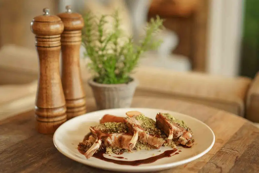 Three lamb chops arranged on a white plate with couscous, vegetables, and a dark jus.