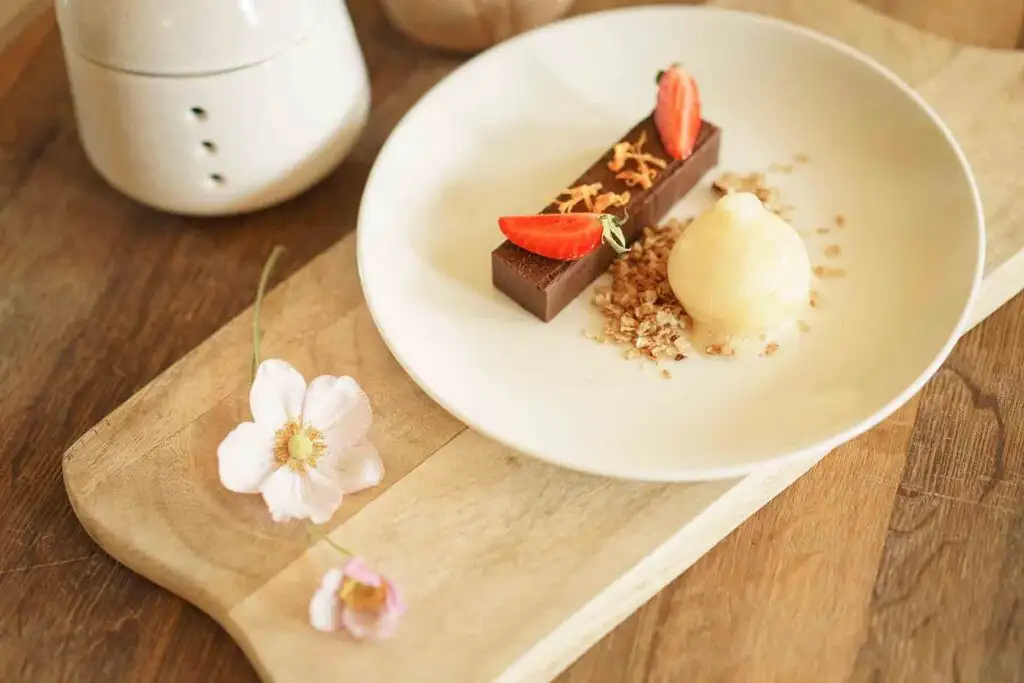 Plated chocolate dessert with vanilla ice cream, strawberry garnish, and nut crumble.