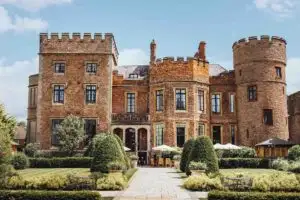 Front view of Rowton Castle in Shropshire with manicured gardens, historic brick façade and castle turrets on a sunny day.