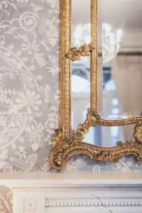 Ornate gilt-framed mirror with intricate floral detailing, set against patterned wallpaper above a classic fireplace in the historic Rowton Castle interior.
