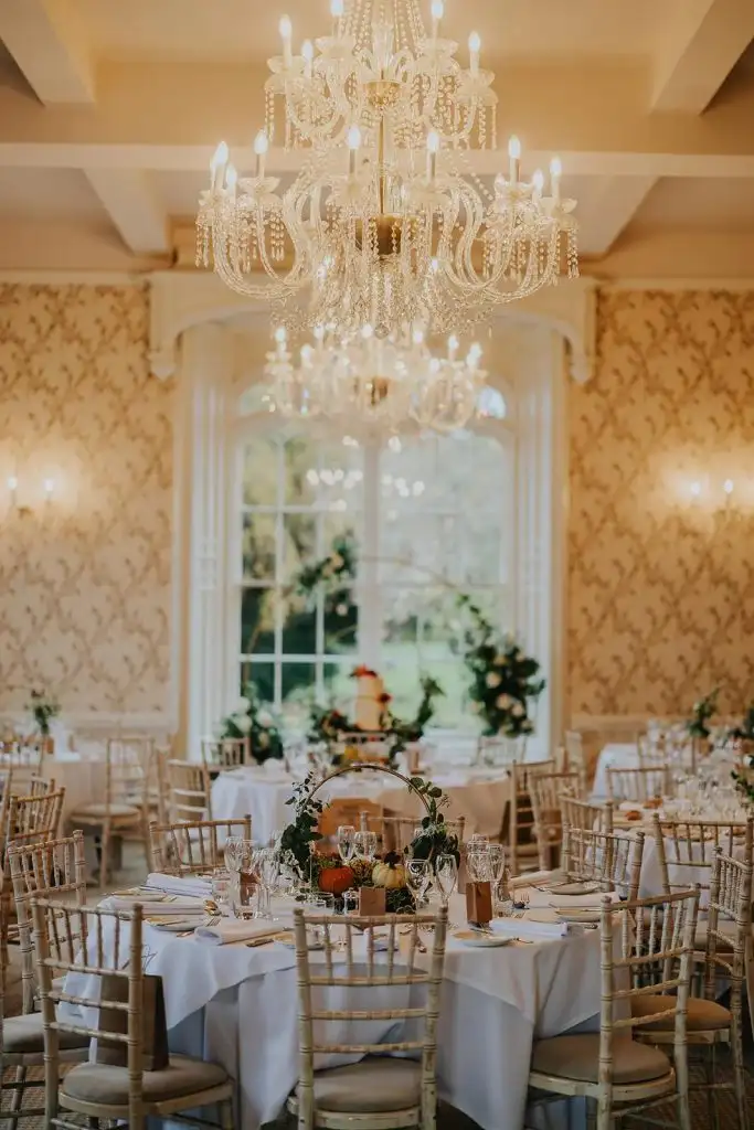 Beautifully decorated wedding reception room at Rowton Castle with crystal chandeliers, round dining tables set with glassware and floral centrepieces, and large windows overlooking the gardens.