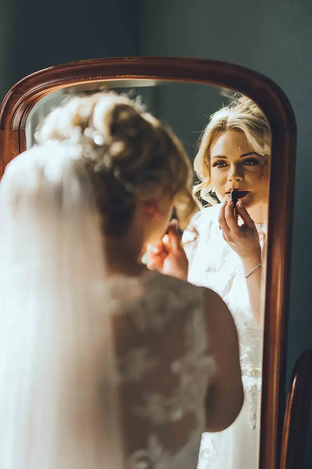 Bride applying lipstick while looking in a mirror