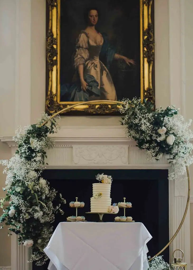 Wedding cake display with floral arch and cupcakes inside Rowton Castle