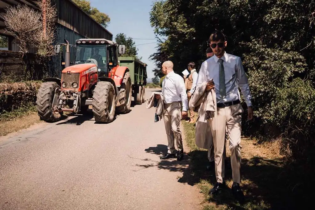Groomsmen walking along a quiet country lane near Rowton Castle, with a red tractor parked beside farm buildings in the rural Shropshire countryside.