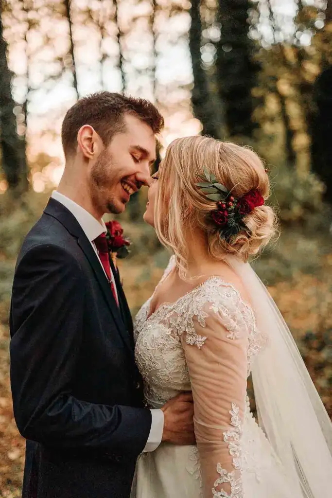 Close-up of a bride and groom smiling and embracing in a woodland setting at Rowton Castle, with warm sunset light filtering through the trees behind them.