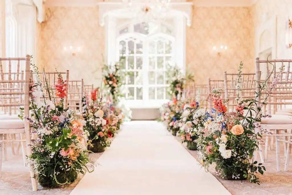 Wedding ceremony setup in Rowton Castle’s indoor ceremony room with floral aisle arrangements and chiavari chairs