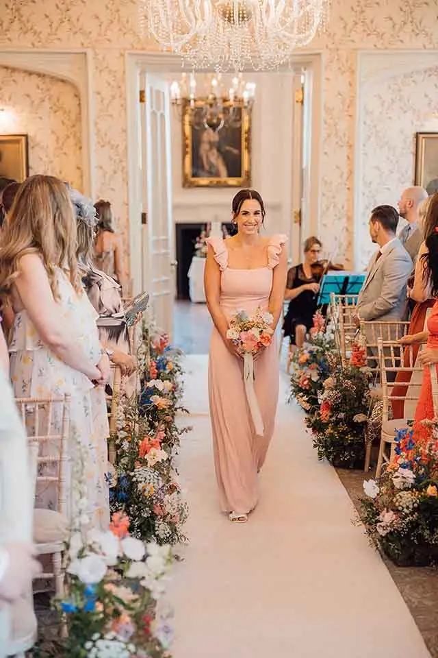Bridesmaid holding a bouquet walking down the aisle during a Rowton Castle wedding ceremony