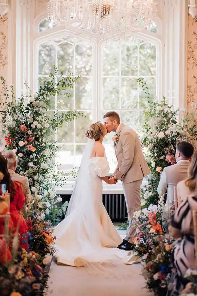 Bride and groom sharing their first kiss during their indoor wedding ceremony at Rowton Castle