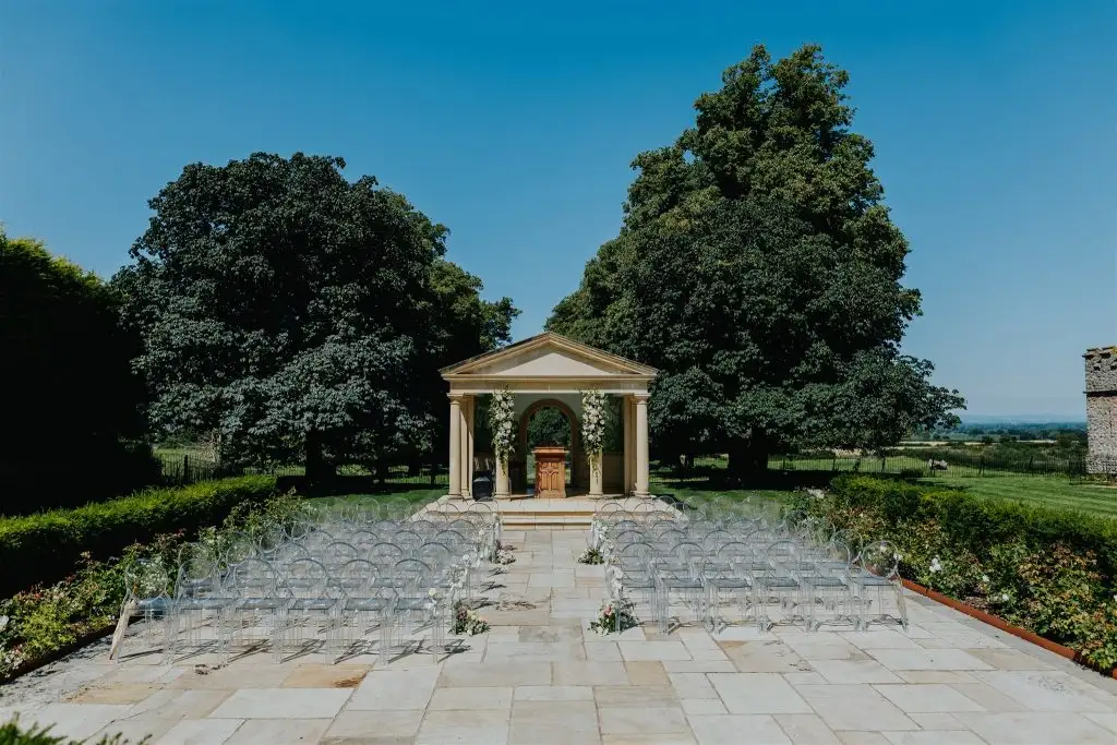 Outdoor wedding ceremony setup at the Rowton Castle temple with clear guest chairs