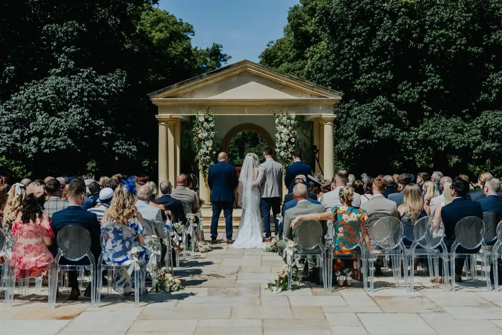 Outdoor wedding ceremony taking place at the Rowton Castle temple with guests seated on clear chairs