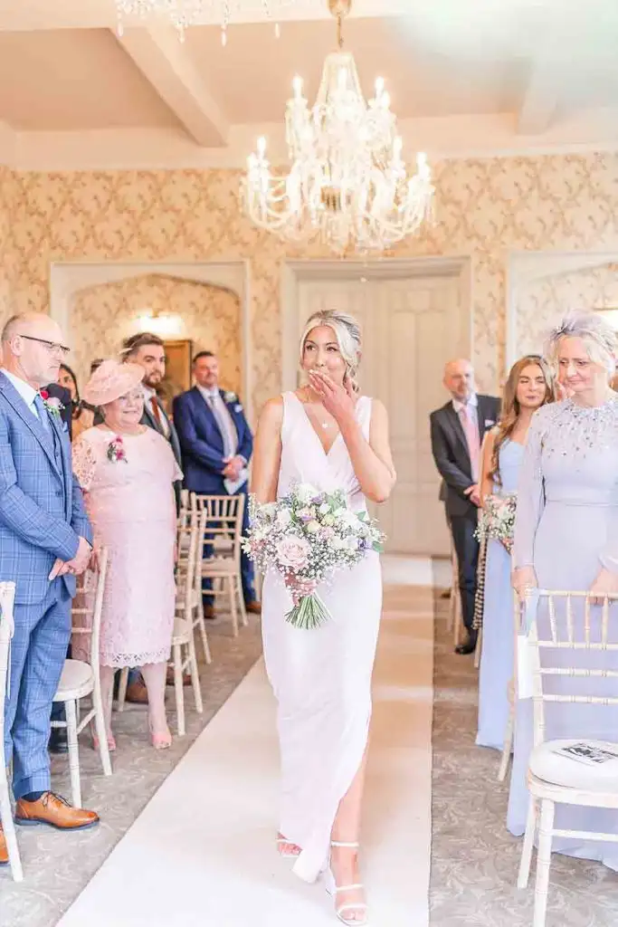 Bride walking down the aisle inside Rowton Castle ceremony room holding a bouquet