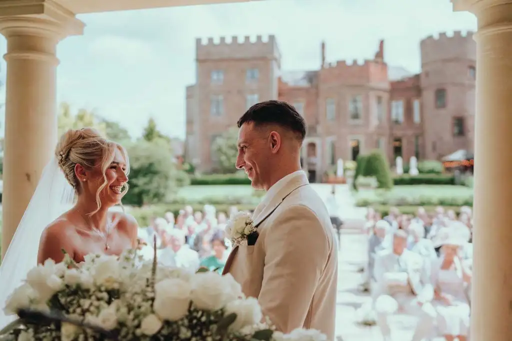 Bride and groom smiling during their outdoor wedding ceremony with Rowton Castle behind them