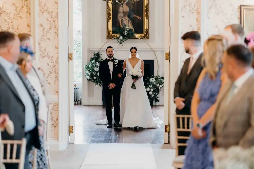 Bride walking down the aisle with her father during an indoor wedding ceremony at Rowton Castle
