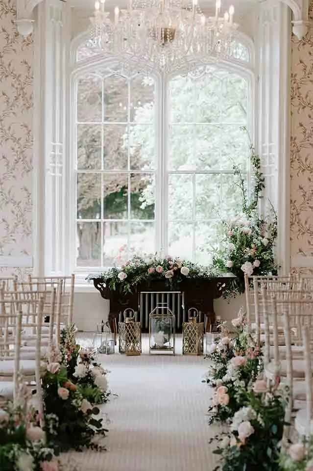 Indoor wedding ceremony setup at Rowton Castle with floral aisle arrangements and chandelier