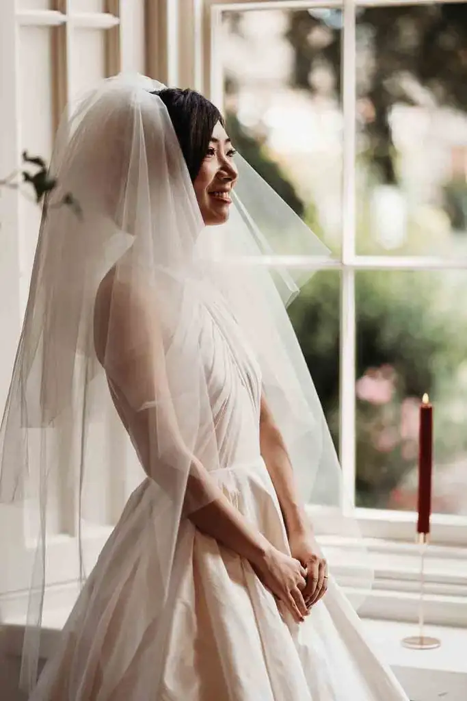 Bride in wedding dress standing beside the ceremony room window at Rowton Castle